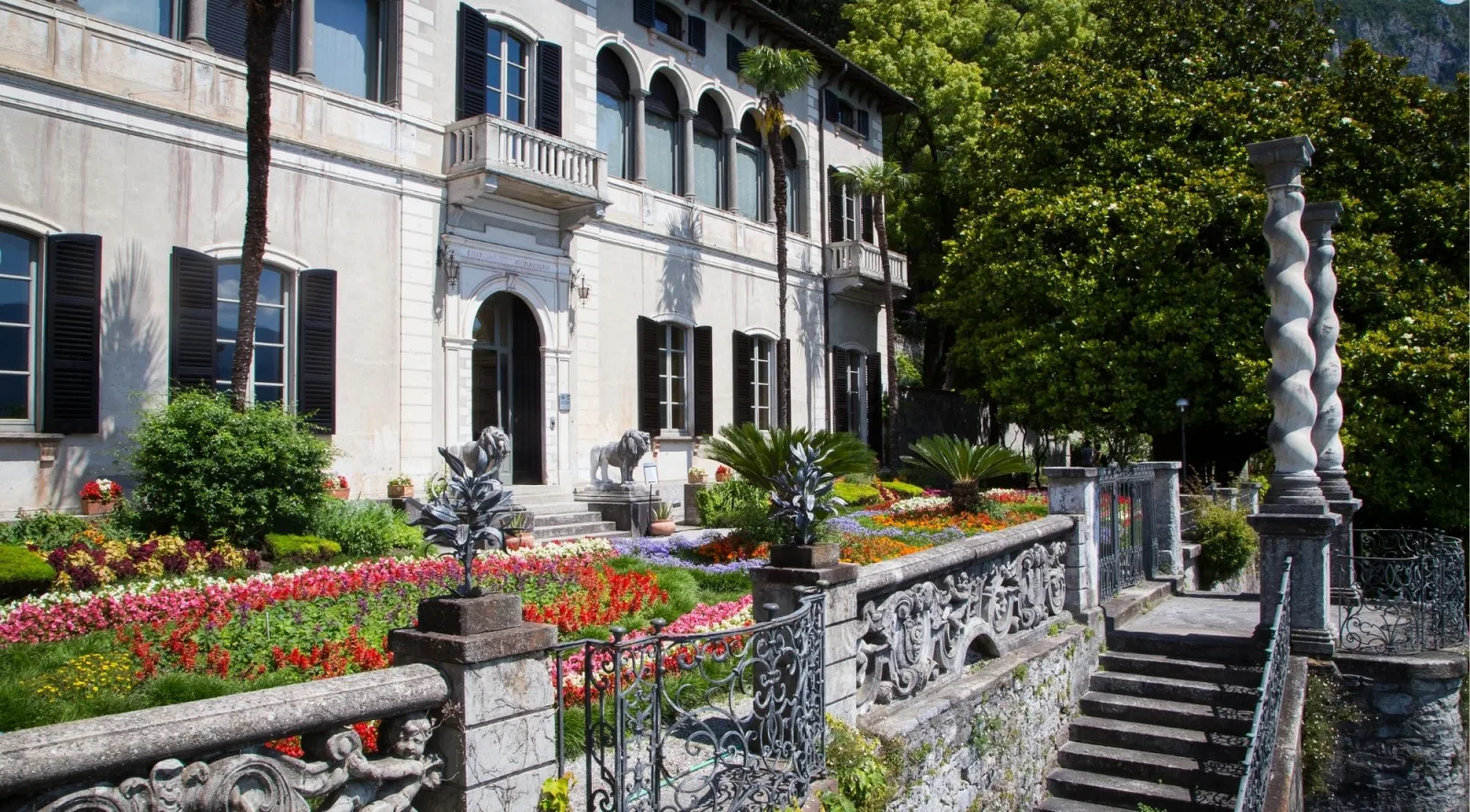 The cream facade of Villa Monastero behind stone lions and a formal parterre of massed spring flowers