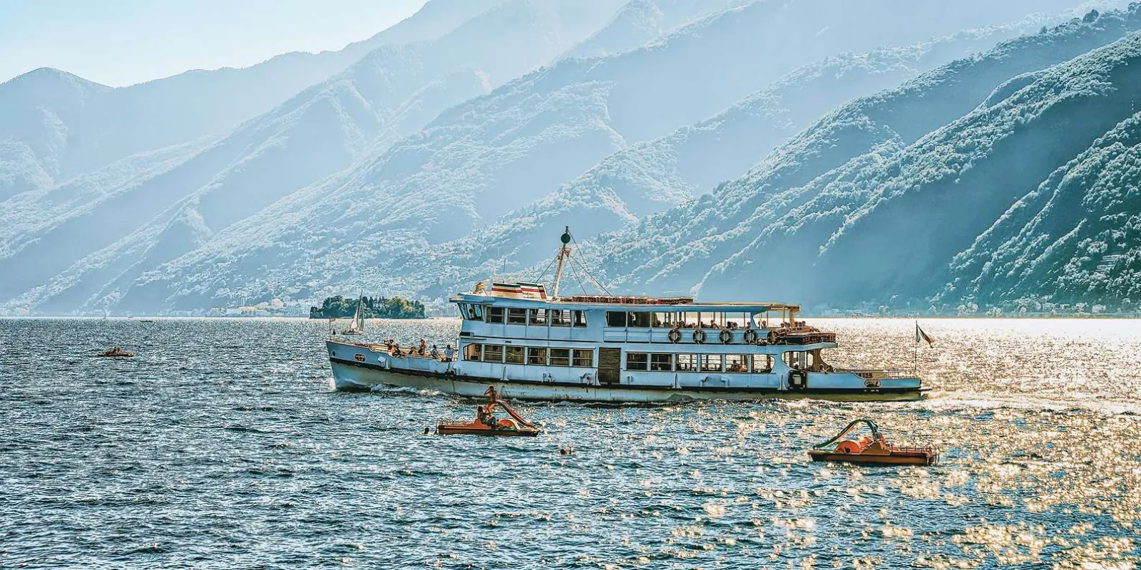 A Lake Como passenger ferry crossing between the villages, the mountains hazy behind