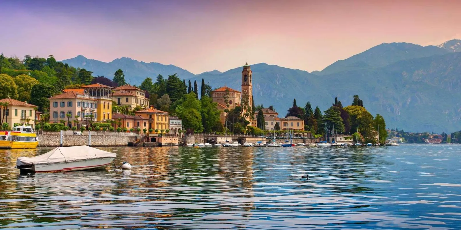 Tremezzina's waterfront at dusk, the bell tower lit against a pink sky