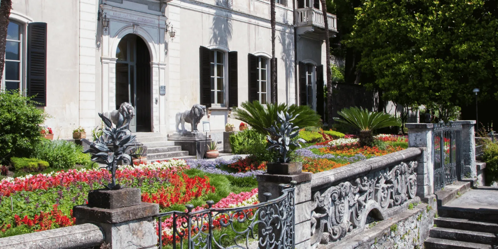 The cream facade of Villa Monastero above its stone lions and a massed parterre of spring flowers