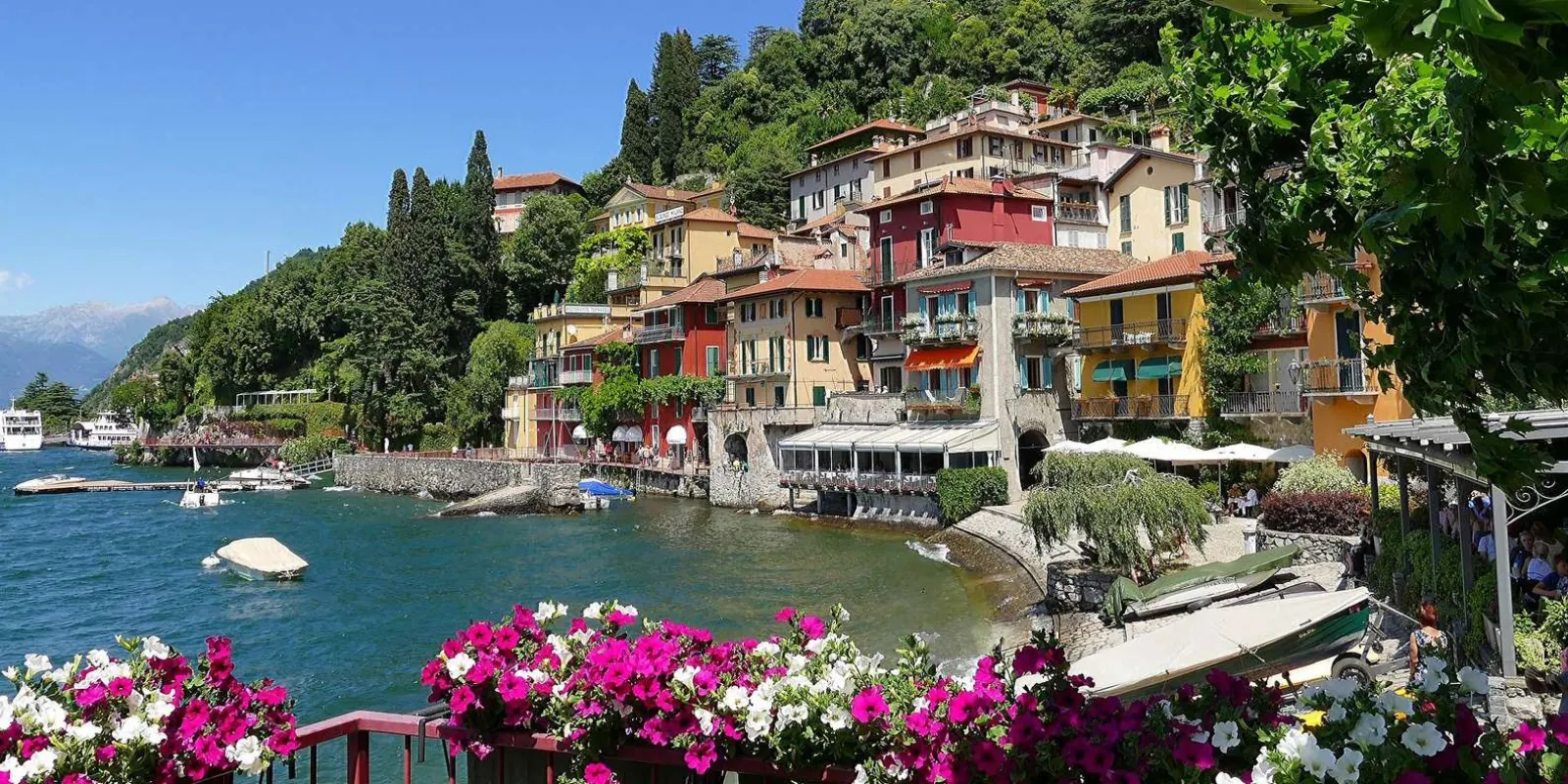 Varenna's harbour from the flower-lined terrace above it, boats drawn up on the little beach